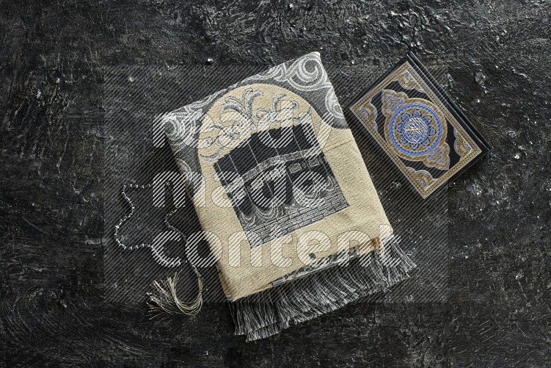 A prayer rug with different elements such as quran and prayer beads on black textured background