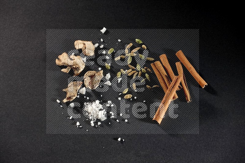 Ginger, salt, cardamom and cinnamon sticks on black flooring