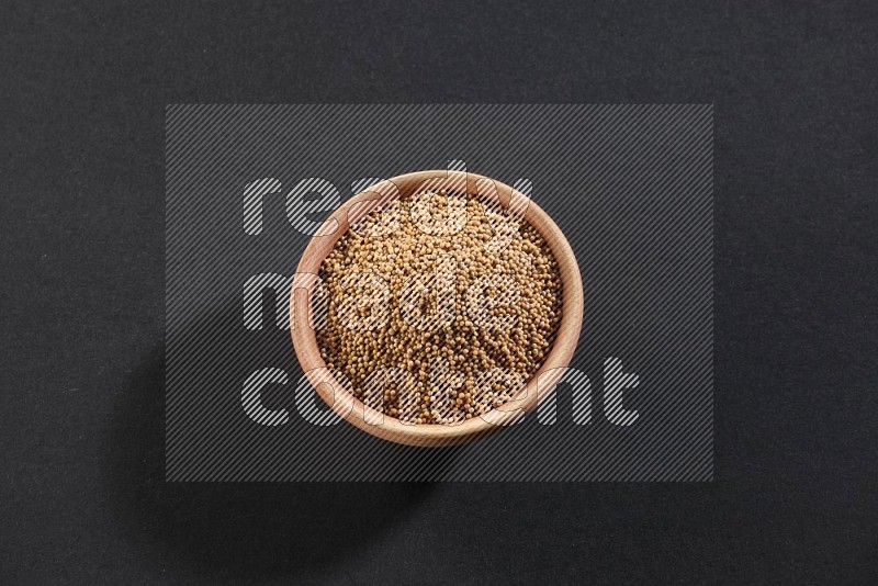 A wooden bowl full of mustard seeds on a black flooring in different angles