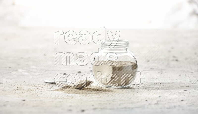 Herbal Glass jar full of white pepper powder and metal spoon full of powder on textured white flooring