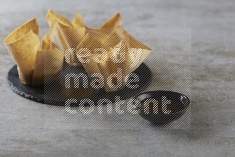 wonton cups with soy sauce ramkin on circle slate on grey textured counter top