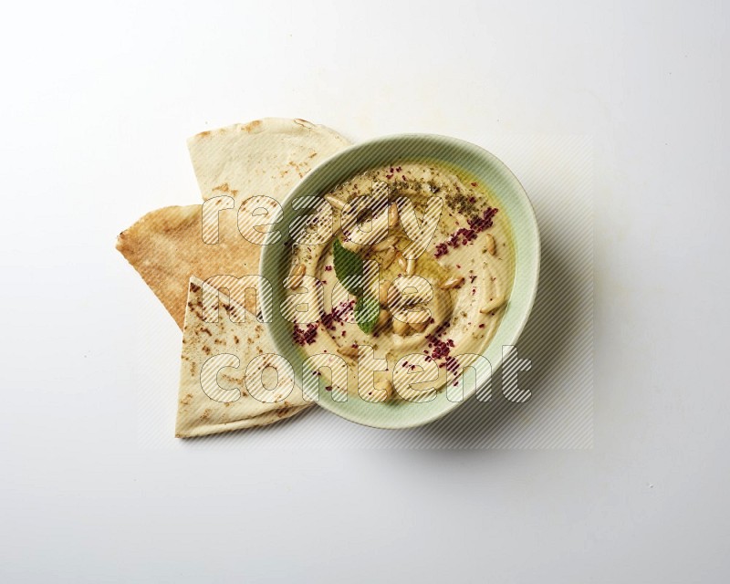 Hummus in a green plate garnished with zattar & sumak on a white background