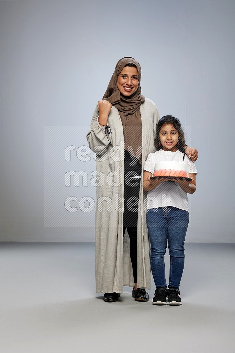 A girl giving a cake to her mother on gray background