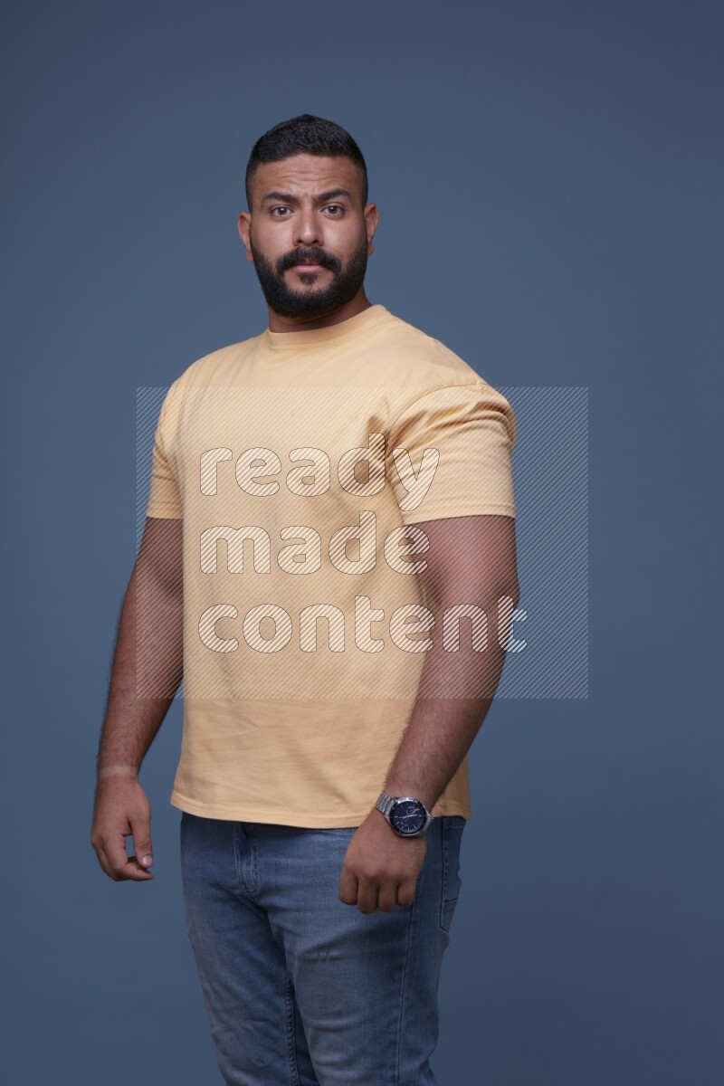 A man posing in a blue background wearing a yellow shirt