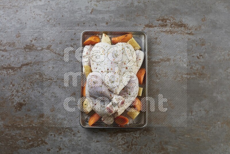 whole Raw chicken on a small oven trey direct on a rustic grey background