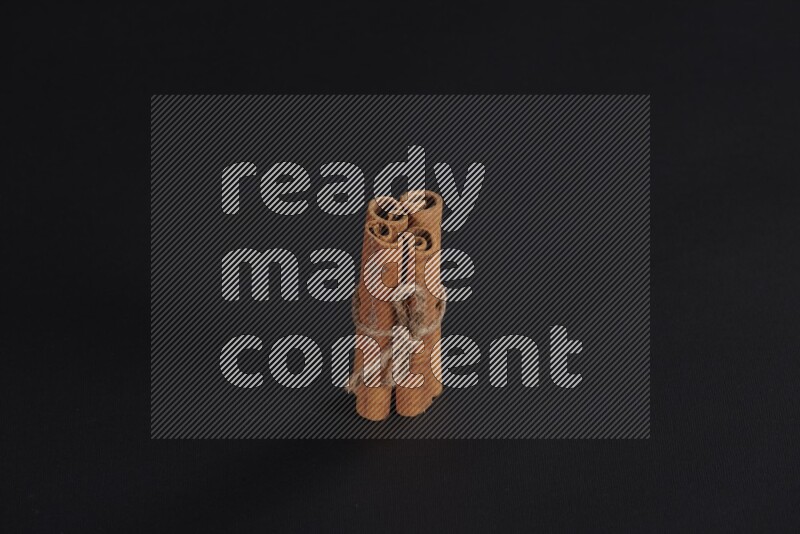 4 Cinnamon sticks stacked and bounded on black flooring