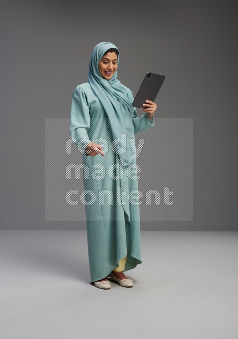 Saudi Woman wearing Abaya standing working on tablet on Gray background