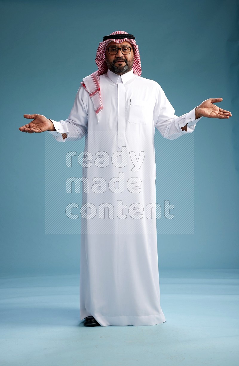 Saudi Man with shimag Standing Interacting with the camera on blue background