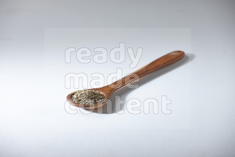 A wooden ladle full of cumin seeds on a white flooring