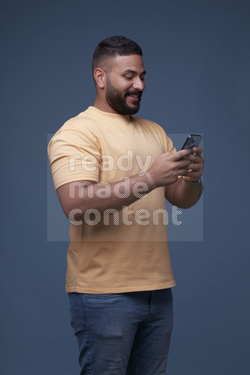 A man Texting on his phone on Blue Background wearing Orange T-shirt