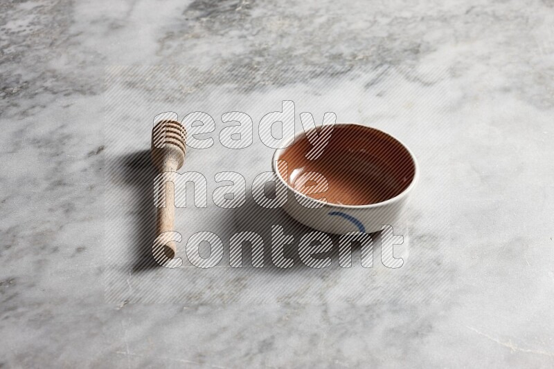 Multicolored pottery bowl with wooden honey dipper on the side on grey marble background