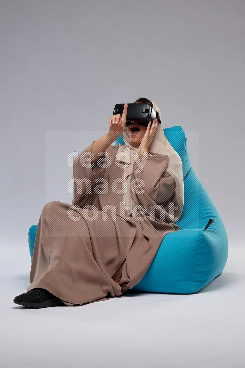A Saudi woman sitting on a blue beanbag and gaming with VR