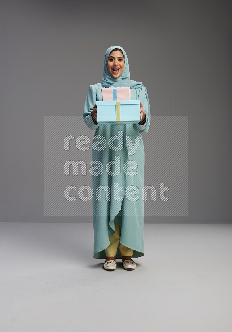 Saudi Woman wearing Abaya standing holding gift box on Gray background