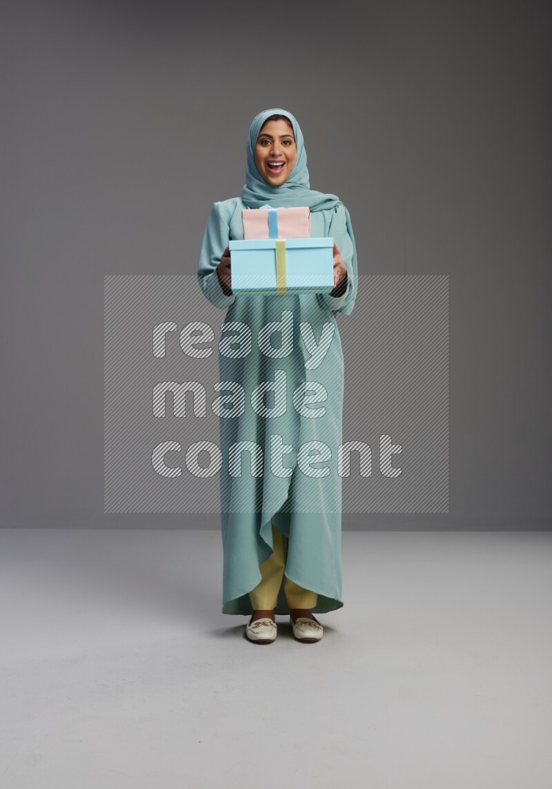 Saudi Woman wearing Abaya standing holding gift box on Gray background