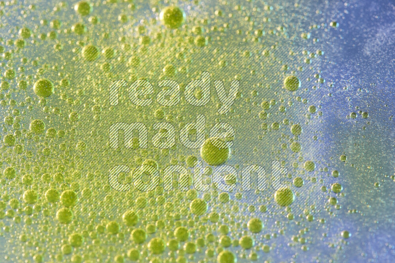 Close-ups of abstract yellow watercolor drops on oil Surface on blue background