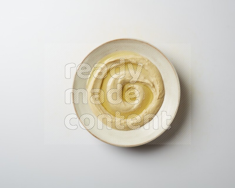 Hummus in a pottry plate garnished with olive oil on a white background