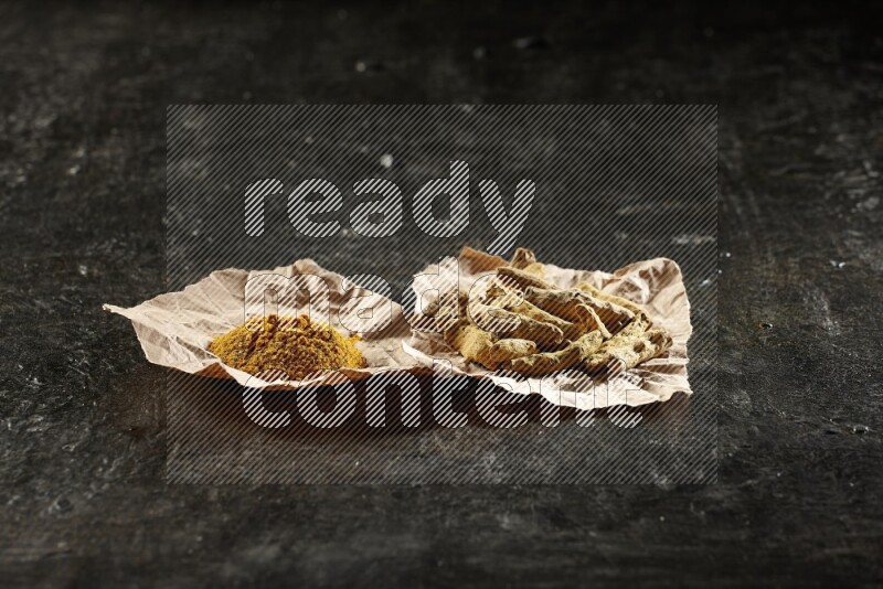 أصابع الكركم المجففة وبودرة الكركم في قطع من الورق على خلفية سوداء