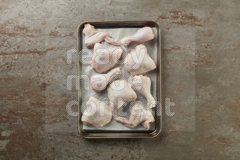 Mixed fresh chicken pieces in an oven tray on a textured rustic background