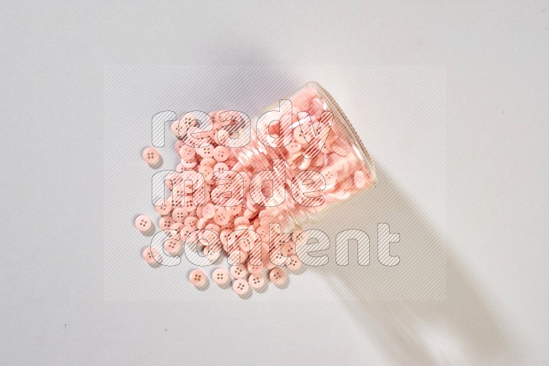 A glass jar full of colored buttons on grey background