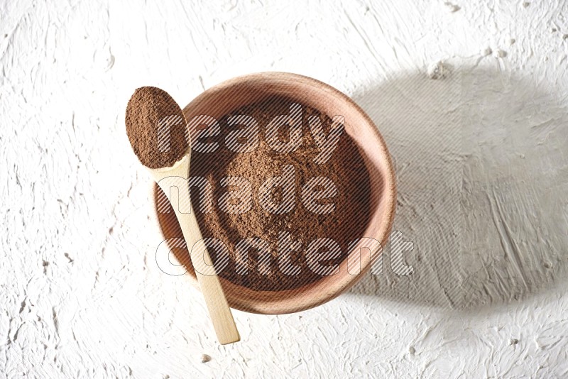 A wooden bowl and a wooden spoon full of cloves powder on a textured white flooring