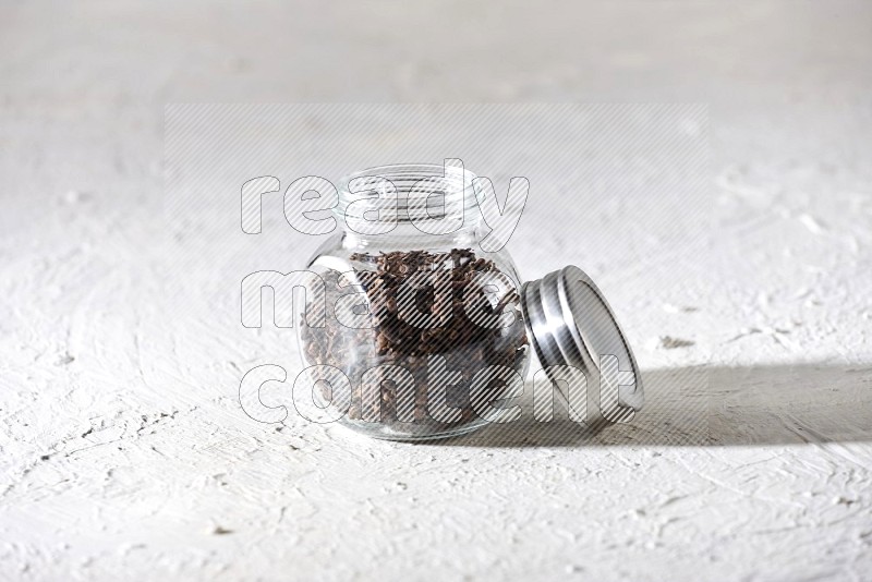 A glass spice jar full of cloves on textured white flooring