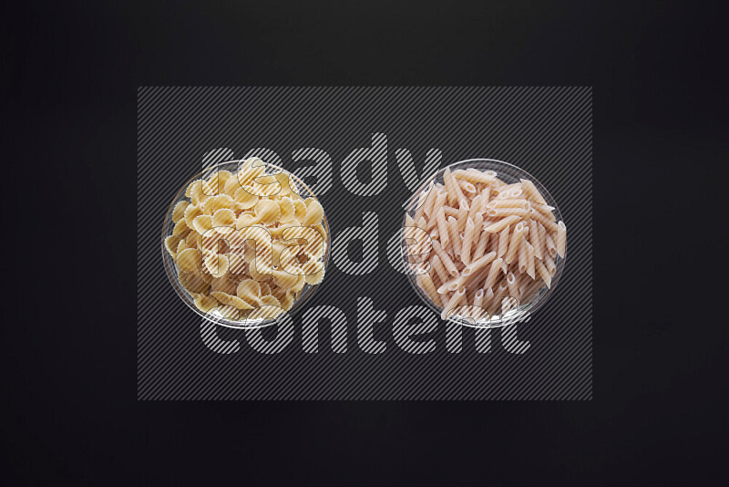 Different pasta types in glass bowls on black background