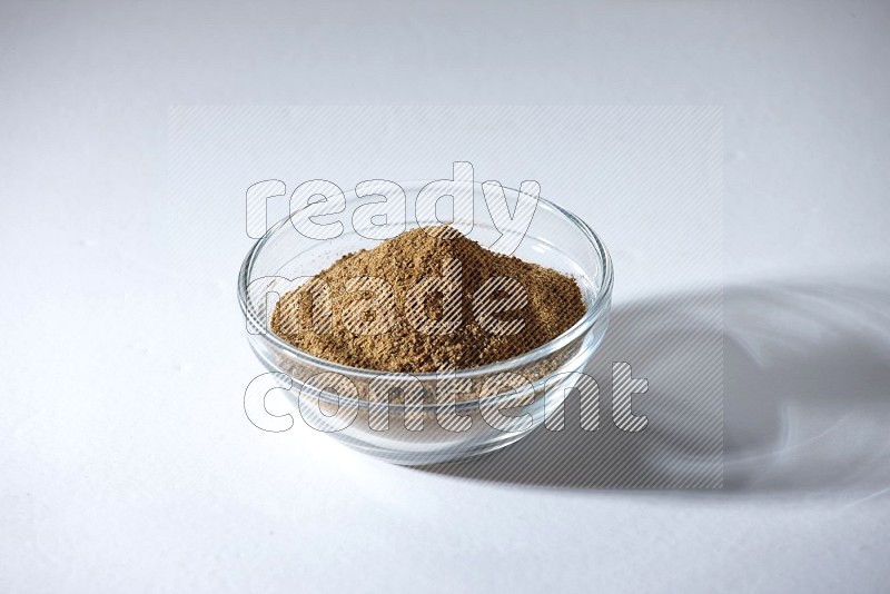 A glass bowl full of cumin powder on a white flooring