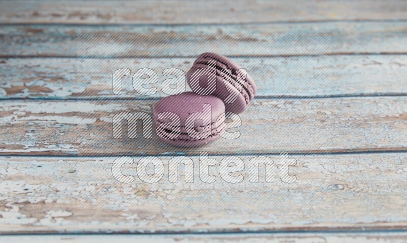 45º Shot of two Purple Blueberry macarons on light blue wooden background