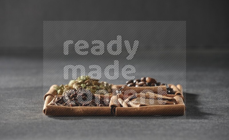 4 مربعات من عيدان القرفة ممتلئة بحبوب القهوة وقطع القرفة والقرنفل وحبوب الهيل على أرضية سوداء