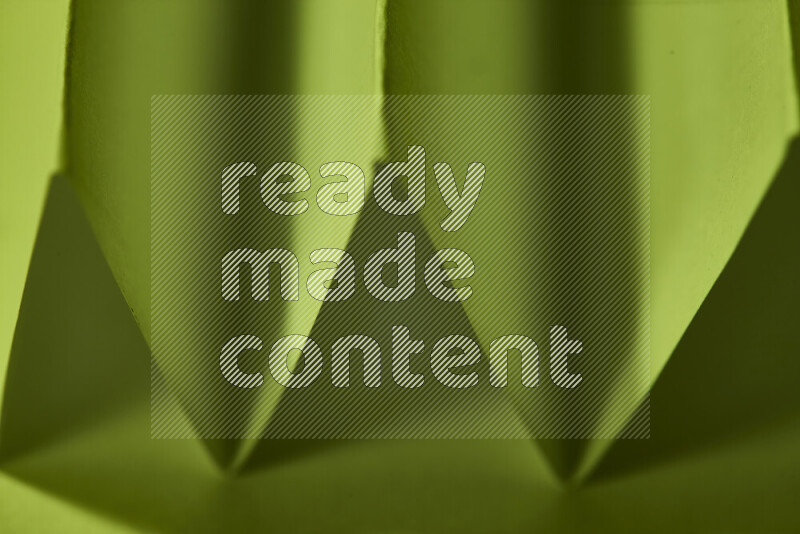 A close-up abstract image showing sharp geometric paper folds in green gradients