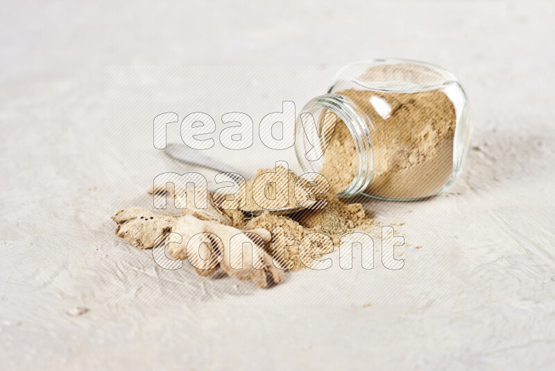 A glass jar full of ground ginger powder flipped with some spilling powder on white background