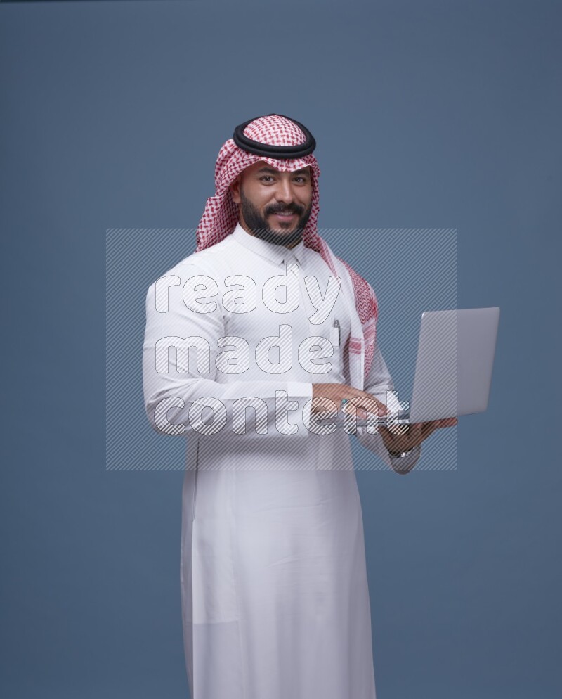 A Saudi man Holding a Laptop on Blue Background wearing Saudi Thob and Shomag
