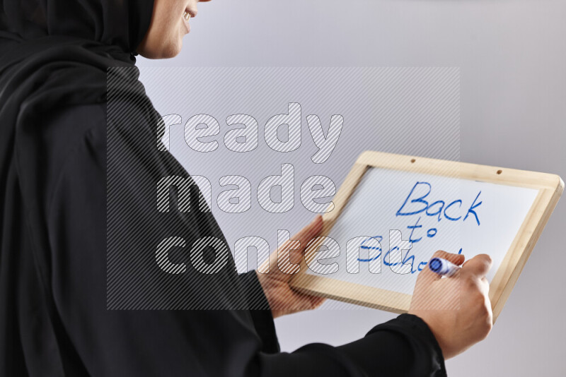 A woman in abaya holding books and a board in different positions (back to school)