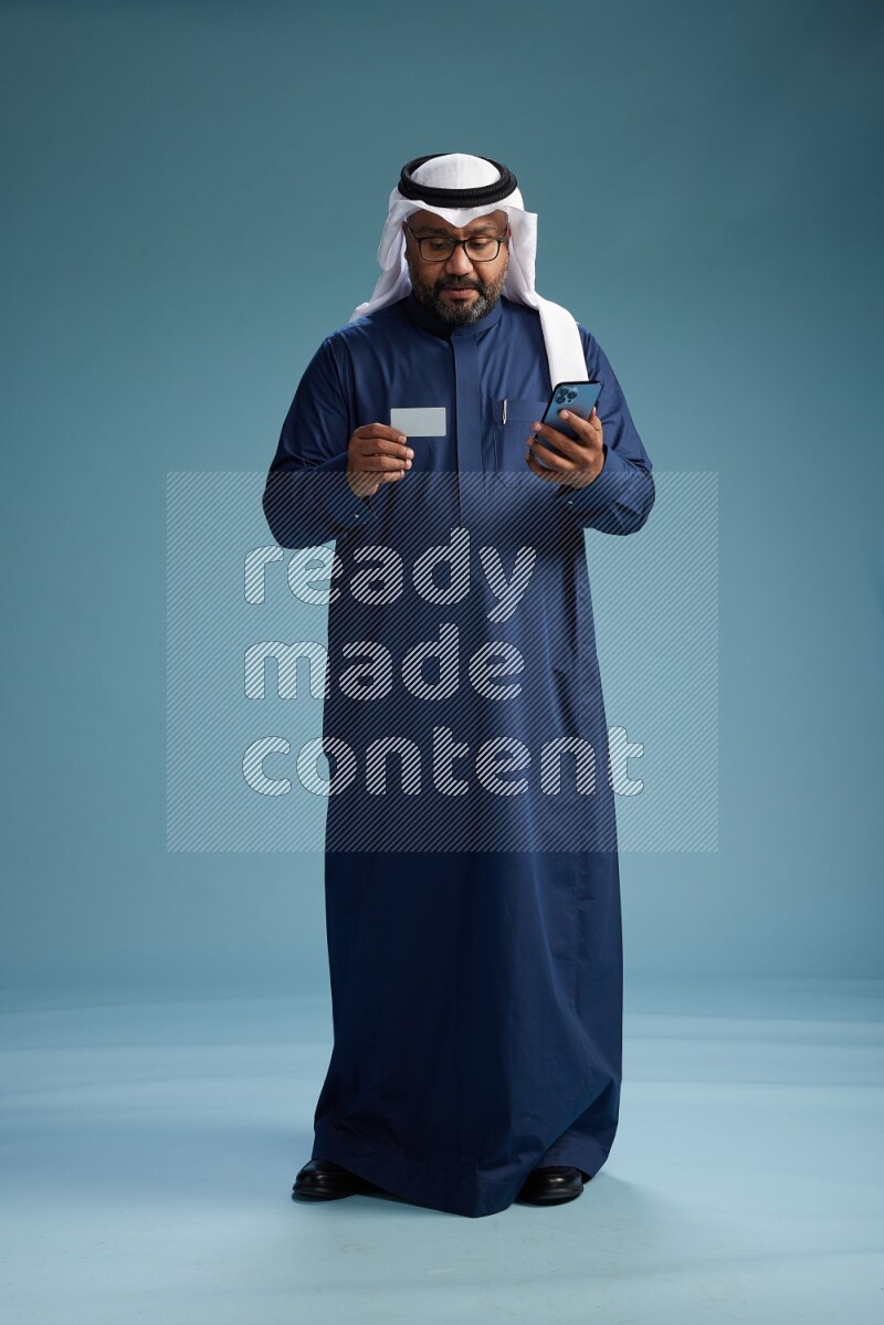 Saudi Man with shimag Standing holding ATM card while talking on phone on blue background