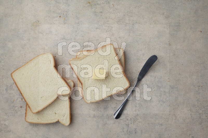 White toast slices with a butter cube and a spreading knife on a light blue textured background