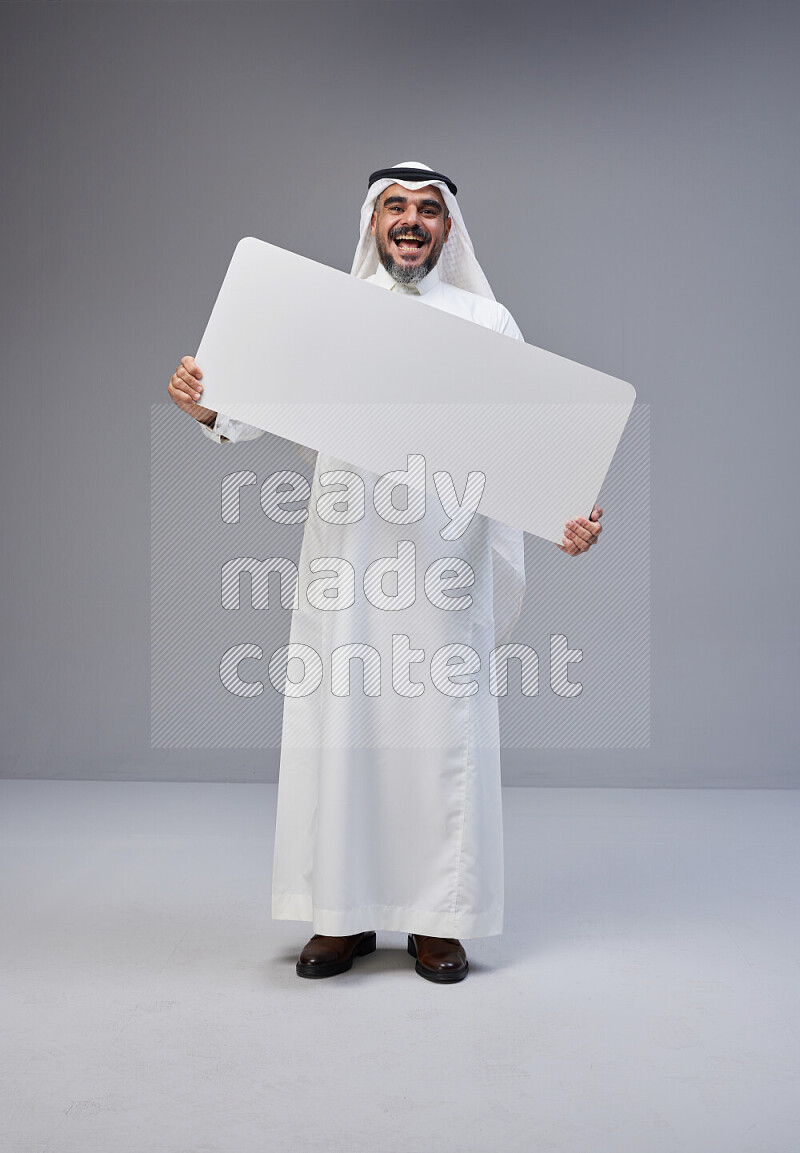 Saudi man Wearing Thob and white Shomag standing holding board on Gray background