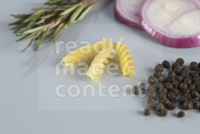 Raw pasta with different ingredients such as cherry tomatoes, garlic, onions, red chilis, black pepper, white pepper, bay laurel leaves, rosemary, cardamom and mushrooms on light blue background