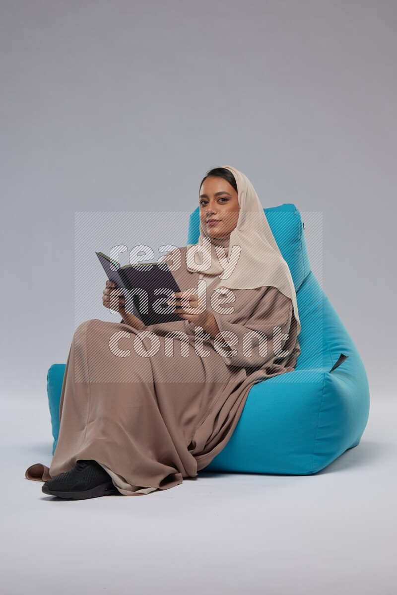 A woman sitting on a blue beanbag and reading a book