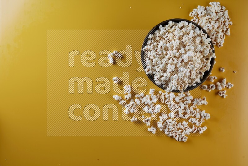 A copper ceramic bowl full of popcorn with popcorn beside it on a yellow background in different angles