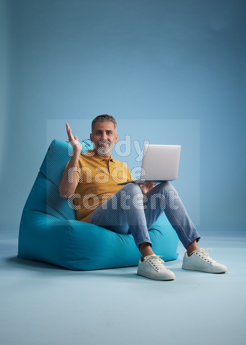 A man sitting on a blue beanbag and working on laptop