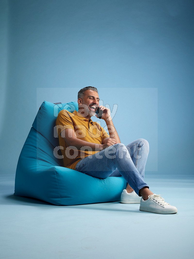 A man sitting on a blue beanbag and talking on the phone