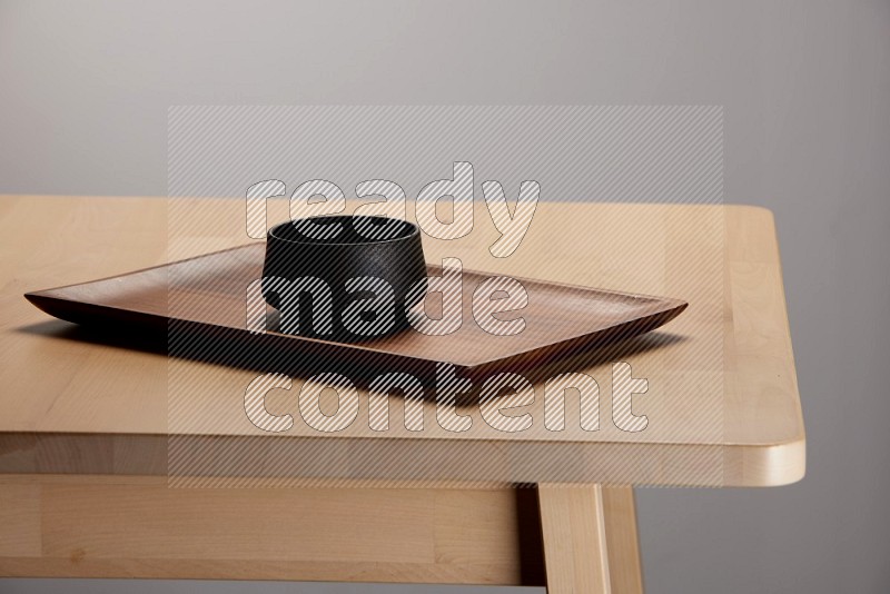 black bowl placed on a rectangular wooden tray on the edge of wooden table