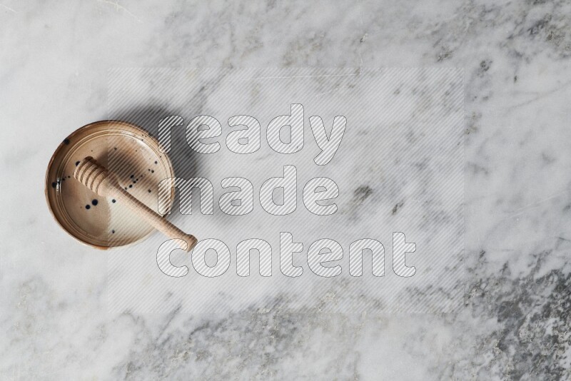 Multicolored pottery bowl with wooden honey dipper in it on grey marble background
