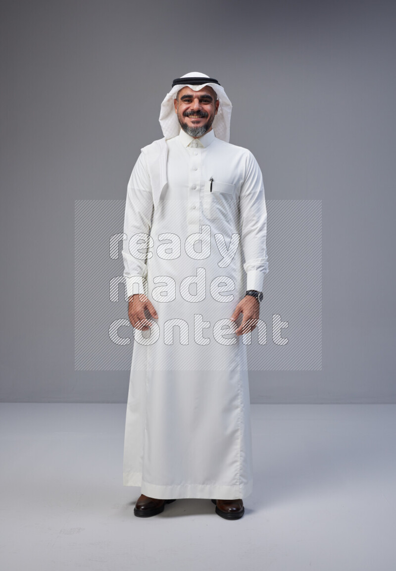 Saudi man Wearing Thob and white Shomag standing interacting with the camera on Gray background