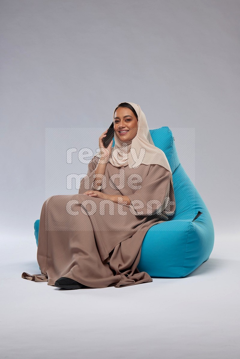 A Saudi woman sitting on a blue beanbag and working on laptop