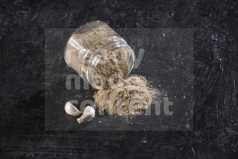 A glass jar full of garlic powder flipped over with the powder came out on a textured black flooring