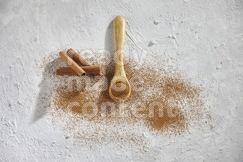 Cinnamon powder in a wooden spoon with cinnamon sticks and sprinkles powder on the flooring on white background