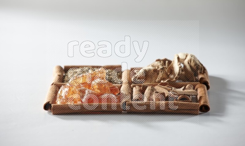 4 مربعات من أعواد القرفة ممتلئة بالكمون والقرفة والزنجبيل المجفف والصمغ العربي على أرضية بيضاء