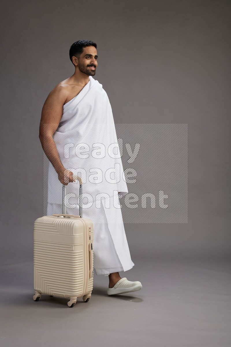 A man wearing Ehram Standing holding traveling bag on gray background