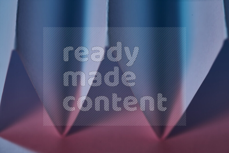 صورة مجردة مقربة تظهر طيات ورقية هندسية حادة بتدرجات اللون الأزرق والوردي